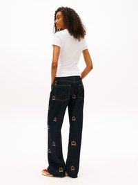 Dark blue denim jeans with embroidered crown motifs, straight-leg design, subtle stitching details, and a relaxed fit. Paired with a white tee.