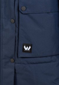 Marinblå isolerad jacka med tryckknappar, med en framträdande svart WHISTLER-logotyp på bröstfickan. Slät yta, slitstark material.