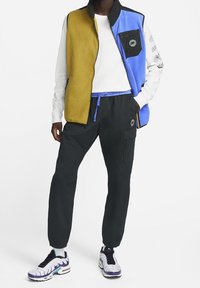 Färgglad fleeceväst i gult, blått och svart med dragkedja och framficka; tillsammans med svarta joggers med sidfickor.