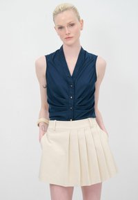 Laivastonsininen ilmanhiha blouse, jossa on kerrostettua yksityiskohtaa ja kultanappeja, yhdistettynä korkeavyötäröiseen, poimutettuun kermaiseen hameeseen, jossa on sivutaskut.