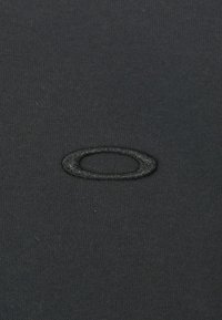 Tissue neagră cu o textură netedă prezintă un logo oval negru brodat. Vedere în apropiere concentrează detaliile de cusătură ale logo-ului.