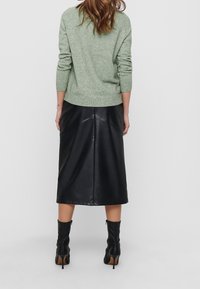 Grüner gestrickter Pullover mit gerippten Bündchen und Saum, kombiniert mit einem schwarzen Leder-Midirock mit Nahtdetails und hohen schwarzen Stiefeln.