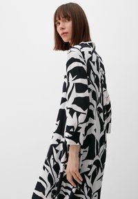 Schwarz-weißes Kleid mit auffälligem Blattmuster, langen Ärmeln, Kragen und fließender Silhouette, aus leichtem Stoff gefertigt.