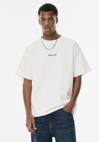 Hvid bomulds oversized t-shirt med teksten "ERROR CODE" i sort, parret med blå denim jeans. Glat tekstur og afslappet pasform.