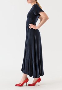 Dlouhé námořnické šaty s vypasovaným korzetem, krátkými rukávy a rozšířeným spodním lemem, v kombinaci s jasně červenými lodičkami na vysokém podpatku s dekoračními detaily.