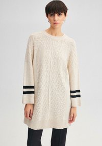 Gebreid sweater in lichtbeige met een geometrisch patroon, featuring ruime mouwen met zwart-witte gestreepte accenten en een ribgebreide onderrand.