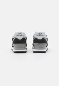 Baskets en suède noir et mesh avec un talon bleu clair, une semelle intermédiaire blanche et une semelle extérieure en caoutchouc foncé. Comprend le logo New Balance à l'arrière.