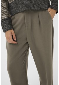 Maglione con un motivo a maglia grigio scuro e testurizzato, abbinato a pantaloni larghi verde oliva con pieghe frontali e tasche laterali.