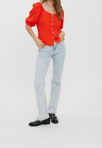 Blouse rouge à manches courtes avec un col en V et une fermeture à boutons, associée à un jean bleu clair et des mocassins noirs. Design simple, texture lisse.