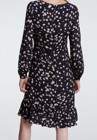 Robe noire à manches longues, motif floral blanc et rouge, ourlet volants et col rond ; le tissu semble léger et fluide.