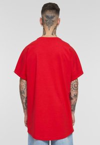 Camiseta roja de gran tamaño con mangas cortas, cuello redondo y un ajuste relajado. Fabricada en algodón con una textura suave. La vista trasera muestra un diseño liso.
