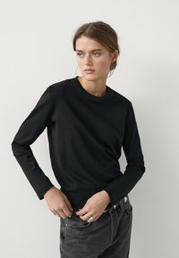 Black long-sleeve shirt made of smooth fabric with a round neckline, paired with high-waisted grey jeans and a simple belt.