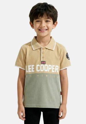 Jeune garçon souriant, portant un polo beige et vert avec le texte "LEE COOPER AUTHENTIC" et un écusson du drapeau Union Jack.