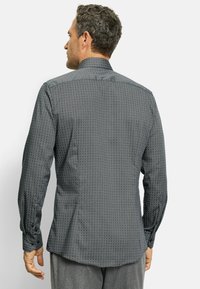 Herrenhemd aus dunkelgrauem Stoff mit geometrischem Muster, langen Ärmeln, Stehkragen und Knopfdetails an den Manschetten.
