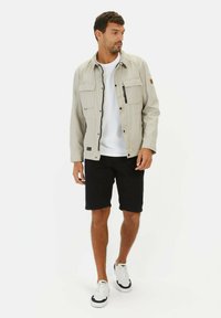 Lys grå jakke med lynlås og trykknap foran, fire lommer, parret med en hvid t-shirt og sorte shorts. Hvide sneakers med sorte detaljer.