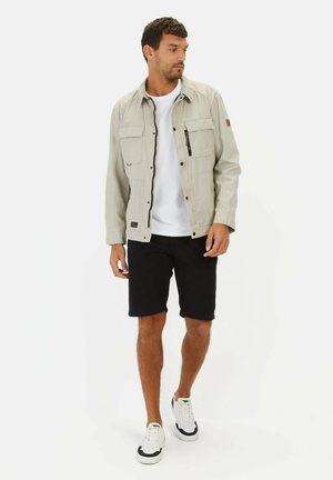 Light grey jacket with a zip and snap front, four pockets, paired with a white t-shirt and black shorts. White sneakers with black accents.