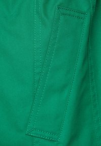 Grön tyg med en strukturfinish och synliga sömmar. Inkluderar en rektangulär ficka på vänster sida, inga ytterligare detaljer.