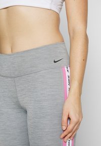 Szare legginsy sportowe o dopasowanym kroju, z kontrastującymi różowymi paskami po bokach oraz czarnym logo na pasku w talii. Gładka tekstura.