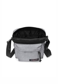 Szara torba na ramię z tkaniny z czarnym zamkiem błyskawicznym, regulowanym paskiem i wewnętrzną podszewką. Posiada małą przednią kieszeń oraz naszywkę z logo marki.