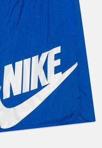 Modré šortky Nike vyrobené z lehkého materiálu, s velkým bílým logem na přední straně, s hladkou texturou a zaobleným lemem.