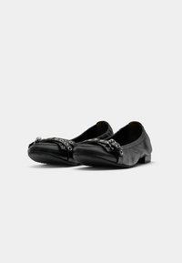 Ballerines en cuir noir avec des sangles en métal sur les orteils, design à bout carré arrondi et talons bas empilés, sur fond blanc.