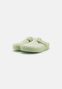 Zöld velúr klumpák sima textúrával, oldalsó csattal és nyitott hátú kialakítással, könnyű gumitalpon. Rendezett, minimalista design.
