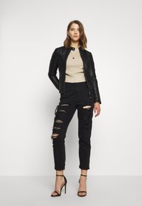 Black leather jacket, beige ribbed sweater, distressed black jeans with large rips, paired with black strappy heels. Simple silver necklace.