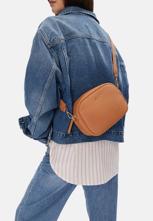 Osoba nosící džínovou bundu a džíny s béžovou koženou kabelkou přes rameno označenou nápisem "JENNY" přes pruhované tričko.