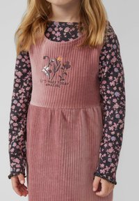 Samtkleid in gedämpftem Pink mit floraler Stickerei; darüber ein langärmliges schwarzes Oberteil mit einem bunten Blumenmuster.