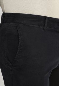 Pantaloni neri in tessuto liscio con una vestibilità su misura, dotati di tasche laterali e una vita piatta, che presentano un design pulito e minimalista.