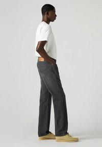 Jeans a righe nere con un taglio dritto, indossati con una t-shirt bianca. Scarpe beige. I jeans presentano un'etichetta sul retro e tasche standard.