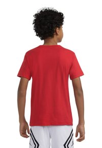 Punane puuvillane T-särk lühikeste varrukatega, ümar kaelus ja sile tekstuur; kantud valgete sportlike šortsidega, millel on mustad aktsendid.