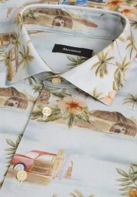Koszula z krótkim rękawem z lekkiego materiału w tropikalny wzór. Posiada beżowe tło, wzory kwiatowe, palmy oraz guziki.