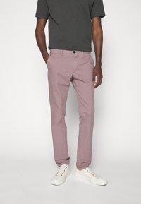 Jasnofioletowe spodnie chino o dopasowanym kroju, wykonane z bawełny. Posiadają pięć kieszeni, zapięcie na guziki oraz miękką strukturę. Połączone z białymi trampkami.