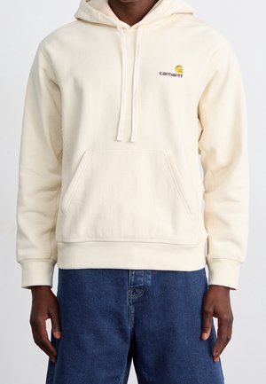 Crème kleurige hoodie van zachte stof, met een voorste kangoeroe zak en een capuchon met trekkoord. "Carhartt" logo in oranje en gele accenten.