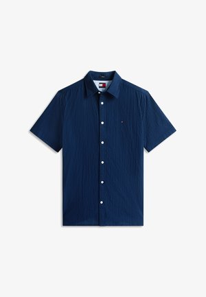 Μπλε ναυτικό πουκάμισο με κοντά μανίκια και κουμπιά, με υφή υφάσματος και μικρό κόκκινο, λευκό και μπλε λογότυπο στο αριστερό στήθος.