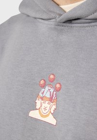 Sudadera gris con un diseño gráfico de múltiples caras que presenta tres cabezas con coronas azules, acentuadas por tres puntos rojos en la parte superior. Textura suave.