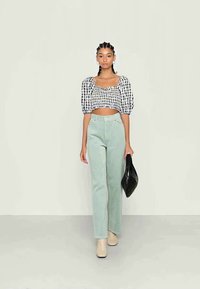 Top cropped xadrez em preto e branco com mangas bufantes, combinado com calças de perna reta verdes claras e botins bejes; segurando uma bolsa preta.