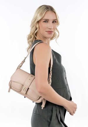 Blush pink leather handbag with gold hardware, frontal flap, and adjustable strap, worn on the shoulder against a grey outfit.