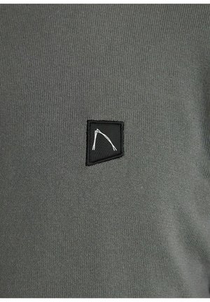 Graues Strickgewebe mit einem kleinen schwarzen Patch, der ein weißes abstraktes Design zeigt. Die Textur ist durchgehend glatt und einheitlich.