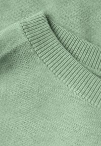 Détail d'un pull tricoté vert clair mettant en valeur un col côtelé et une texture douce ; tissu étroitement tricoté avec une finition lisse.