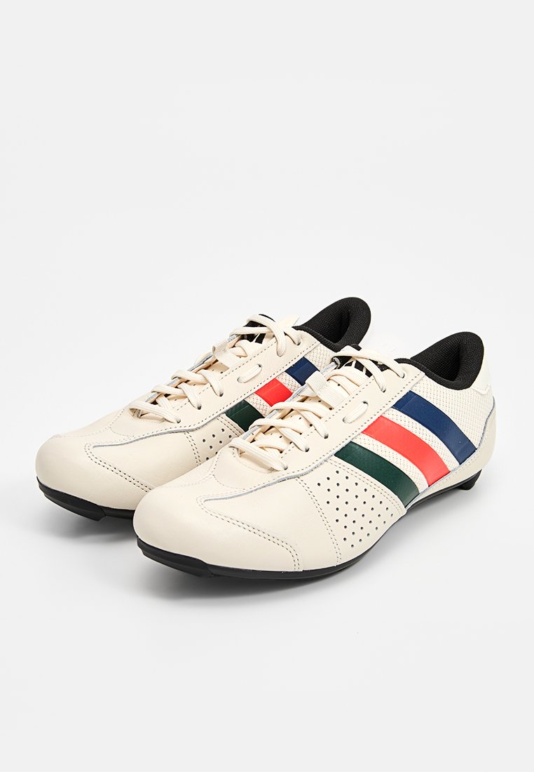 Kremowe buty sportowe z czarnym wnętrzem, z paskowanymi akcentami w kolorze czerwonym, zielonym i niebieskim oraz perforowanymi detalami po bokach.