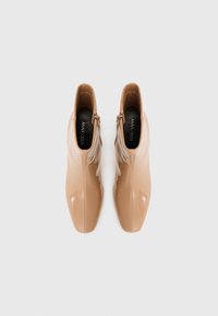 Botines de charol en color piel con un diseño elegante de punta afilada. Presentan cremalleras laterales, textura suave y un brillo sutil.