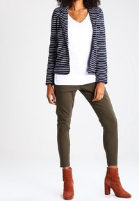 Blazer rayé marine sur une chemise blanche à col en V, associé à un pantalon vert olive et des bottines à cheville couleur rouille. Tissu texturé, coupe ajustée.