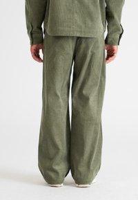 Olive green corduroy outfit featuring wide-leg trousers and a matching button-up jacket, highlighting textured fabric and relaxed fit.