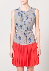 Šaty bez rukávů s šedým vrškem s potiskem modrých a růžových ptáků a plisovanou červenou sukní. Materiál vypadá lehký a splývavý.