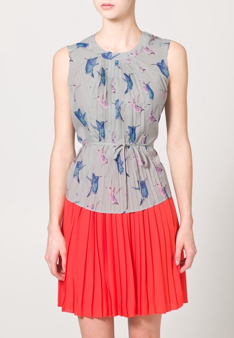 Šaty bez rukávů s šedým vrškem s potiskem modrých a růžových ptáků a plisovanou červenou sukní. Materiál vypadá lehký a splývavý.