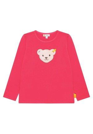 T-shirt enfant à manches longues rose avec un appliqué visage d'ours en peluche beige souriant au centre et une petite étiquette jaune sur la couture latérale.