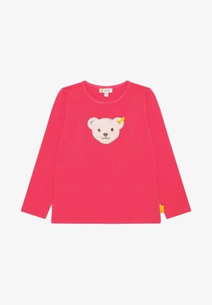 T-shirt enfant à manches longues rose avec un appliqué visage d'ours en peluche beige souriant au centre et une petite étiquette jaune sur la couture latérale.