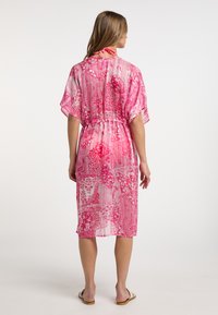 Rožinė raštuota suknelė su kimono rankovėmis, prisiūta liemeniu ir kaklo raiščiu, pagaminta iš lengvos, permatomos medžiagos, iki kelių ilgio.